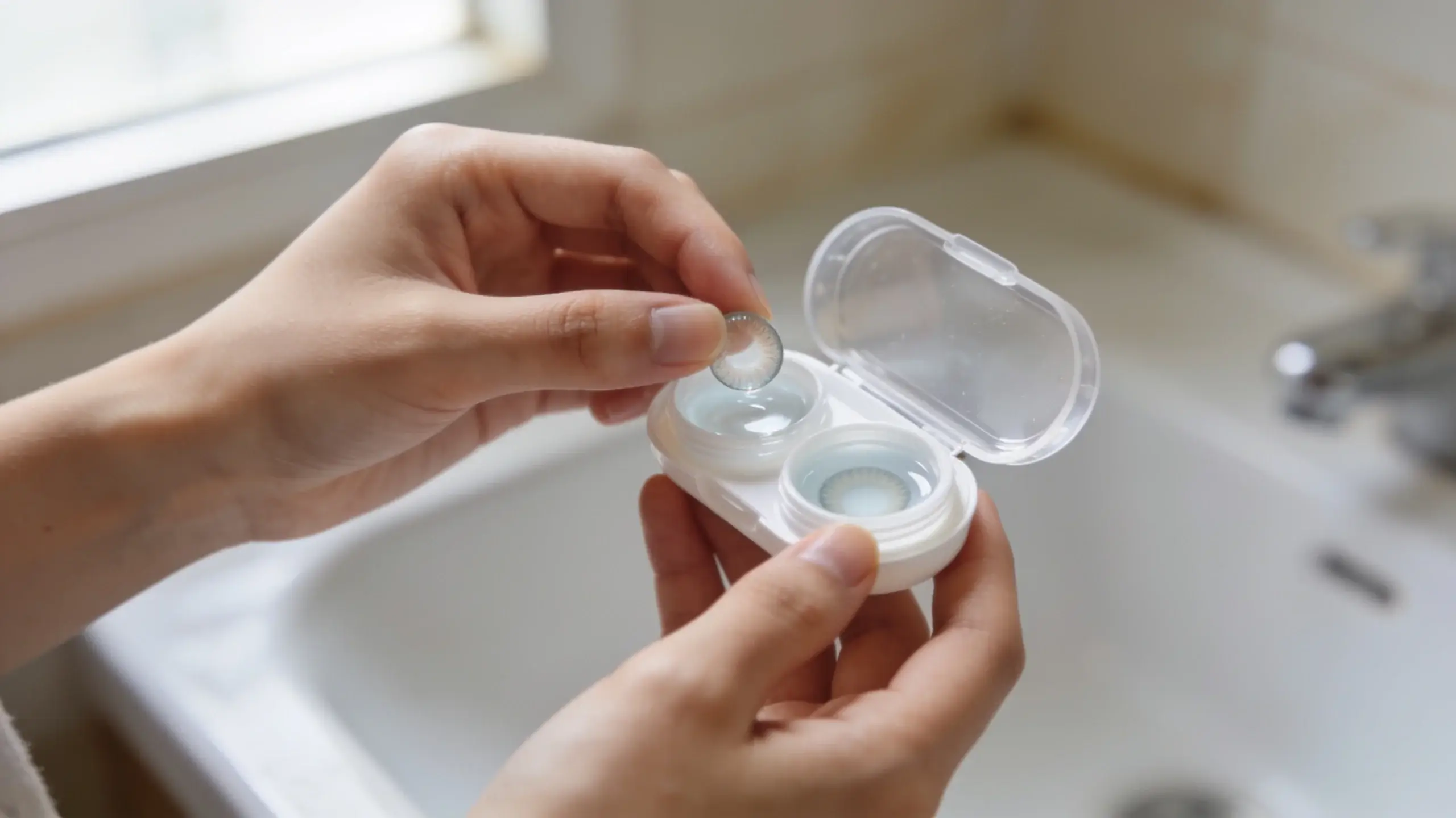 Ruky nad umývadlom vkladajú kontaktnú šošovku do puzdra s čerstvým dezinfekčným roztokom pri hygiene